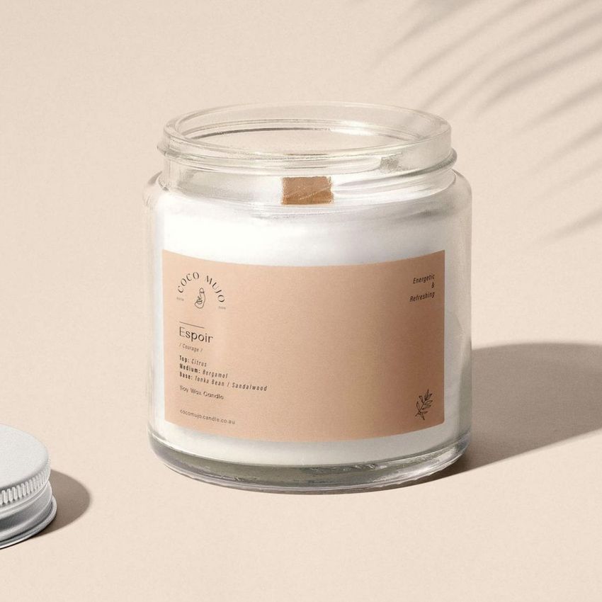 Minimalist candle mockup in a clear glass jar with a beige label, photographed on a neutral, softly shadowed background.