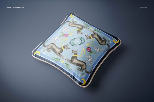 Silk cushion mockup with braided trim, decorated with illustrated dogs, birds, and plants on a blue surface.