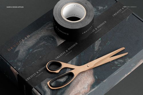 Mailing box mockup with black decorative tape and metallic scissors placed on a dark surface, viewed from above.