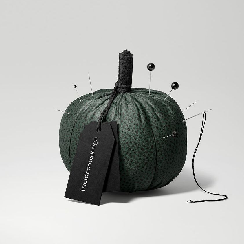 Fabric pumpkin mockup in dark green with subtle dotted pattern, used as a pincushion with pins and needles, on a light background.