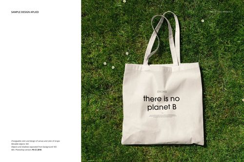 Natural canvas tote bag mockup with black text design, displayed on green grass from a top-down perspective.