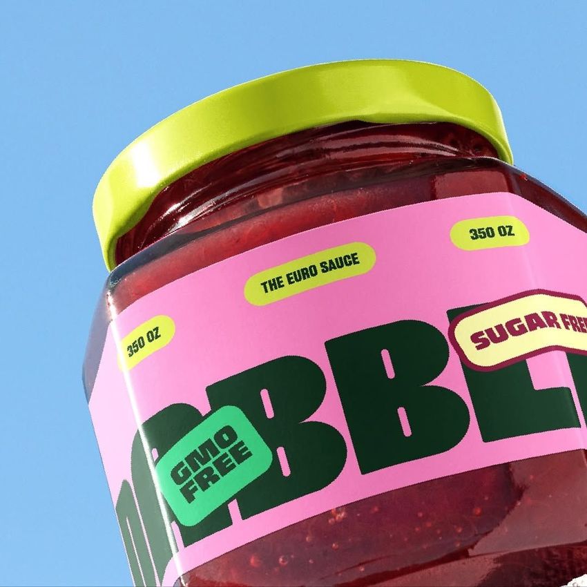 Close-up of a strawberry jam jar mockup with a bright pink and green label, yellow lid, and blue sky background.