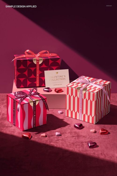 Front view of magnetic gift boxes mockup with ribbons, geometric designs, and assorted chocolates on a pink background.