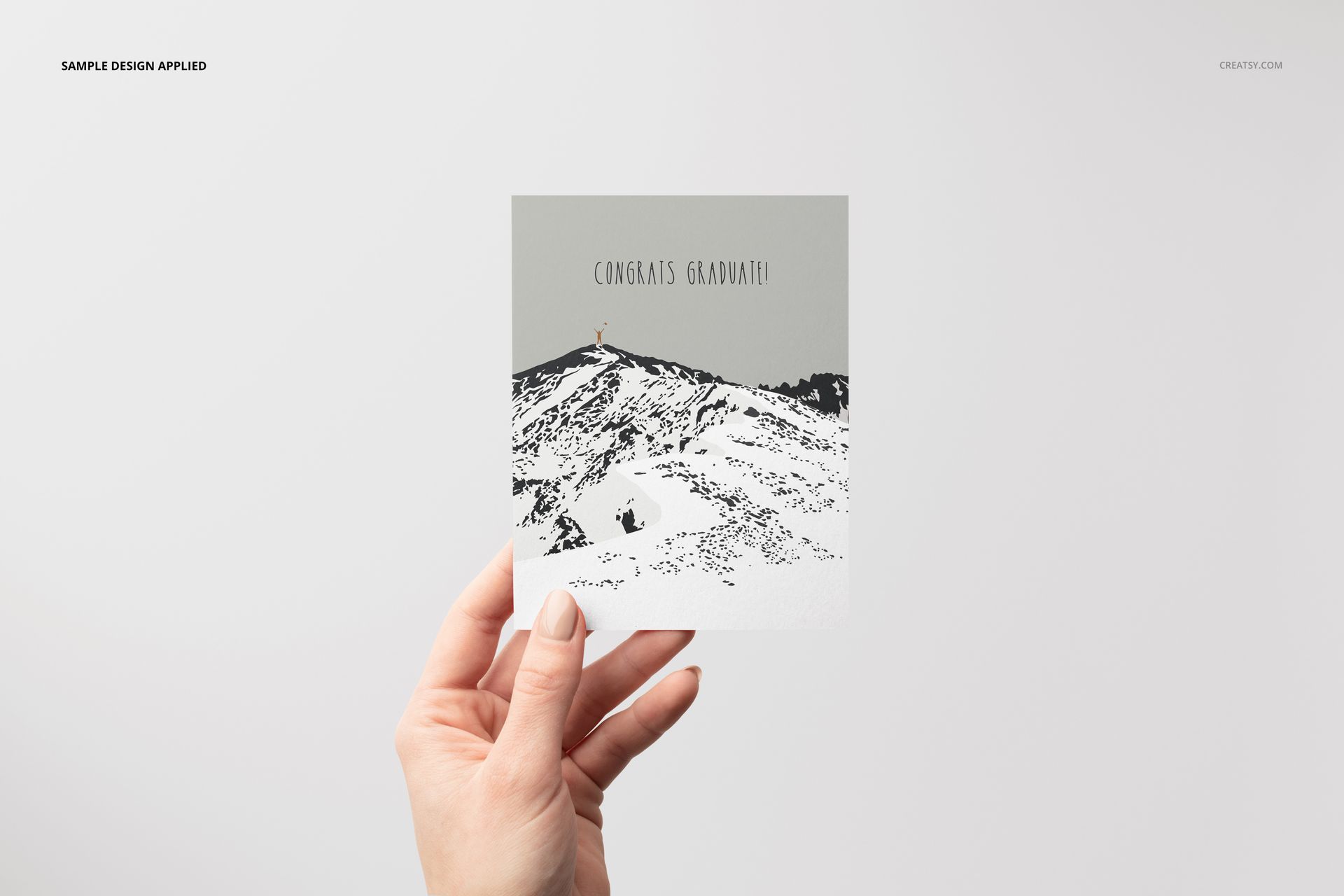 A2 card mockup with a simple mountain pattern and congratulatory text, held up by a hand on a neutral backdrop.