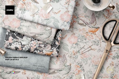 PSD mockup showing folded textiles in soft colors and botanical prints, arranged with scissors and decorative props.
