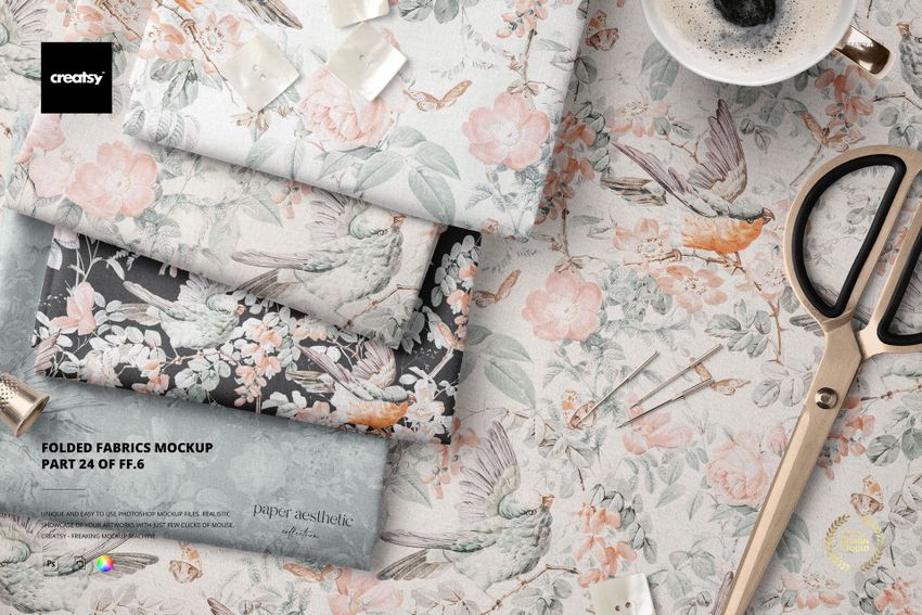 PSD mockup showing folded textiles in soft colors and botanical prints, arranged with scissors and decorative props.