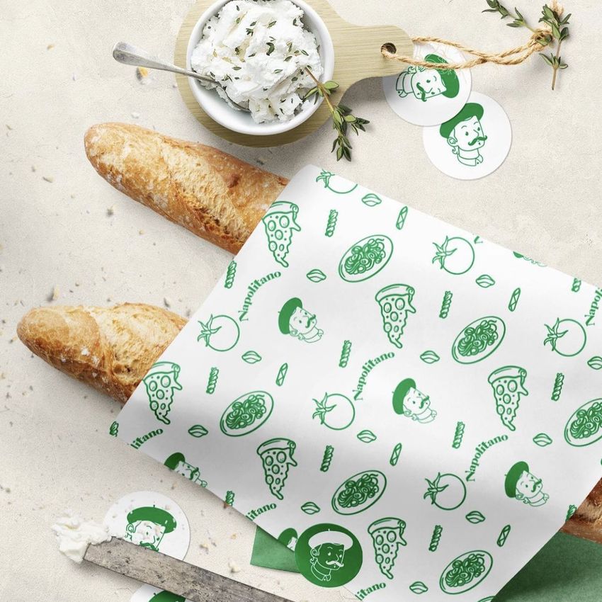 Bakery food safe paper mockup with green illustrated patterns and text overlay, wrapping a baguette on a light surface.