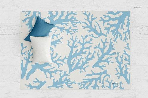 Top view of a woven rug mockup featuring a white surface with blue coral design and two pillows placed on top.