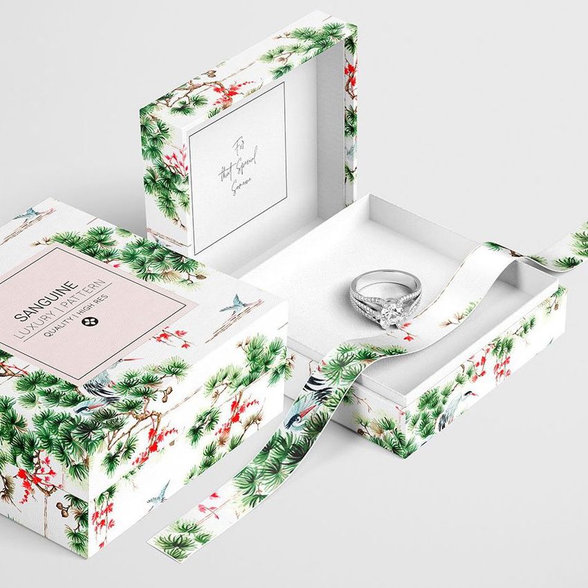 Jewelry box mockup featuring a botanical pattern with green foliage and birds, shown open with a ring inside on a light surface.