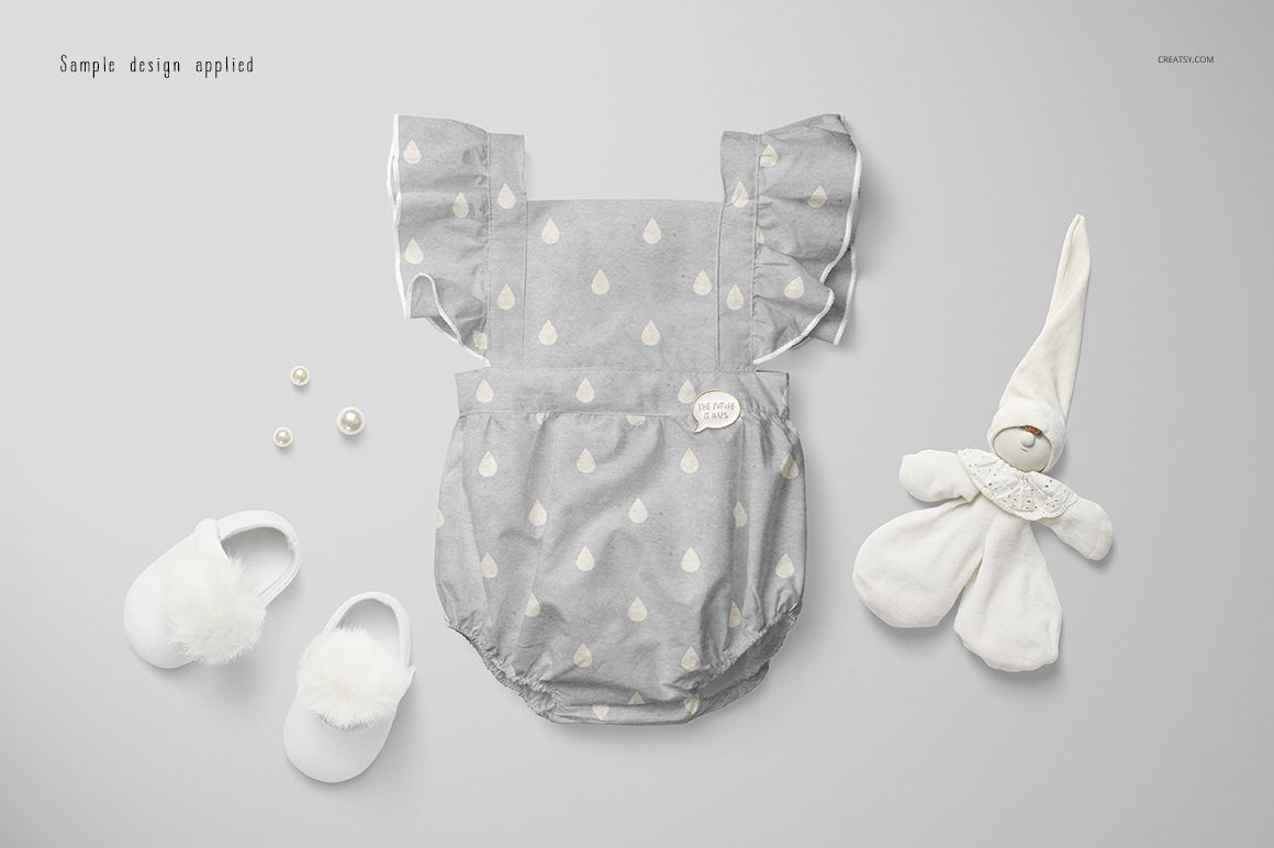 Gray baby romper mockup with white drop shapes, flanked by soft baby shoes, plush toy, and small pearls on a light background.