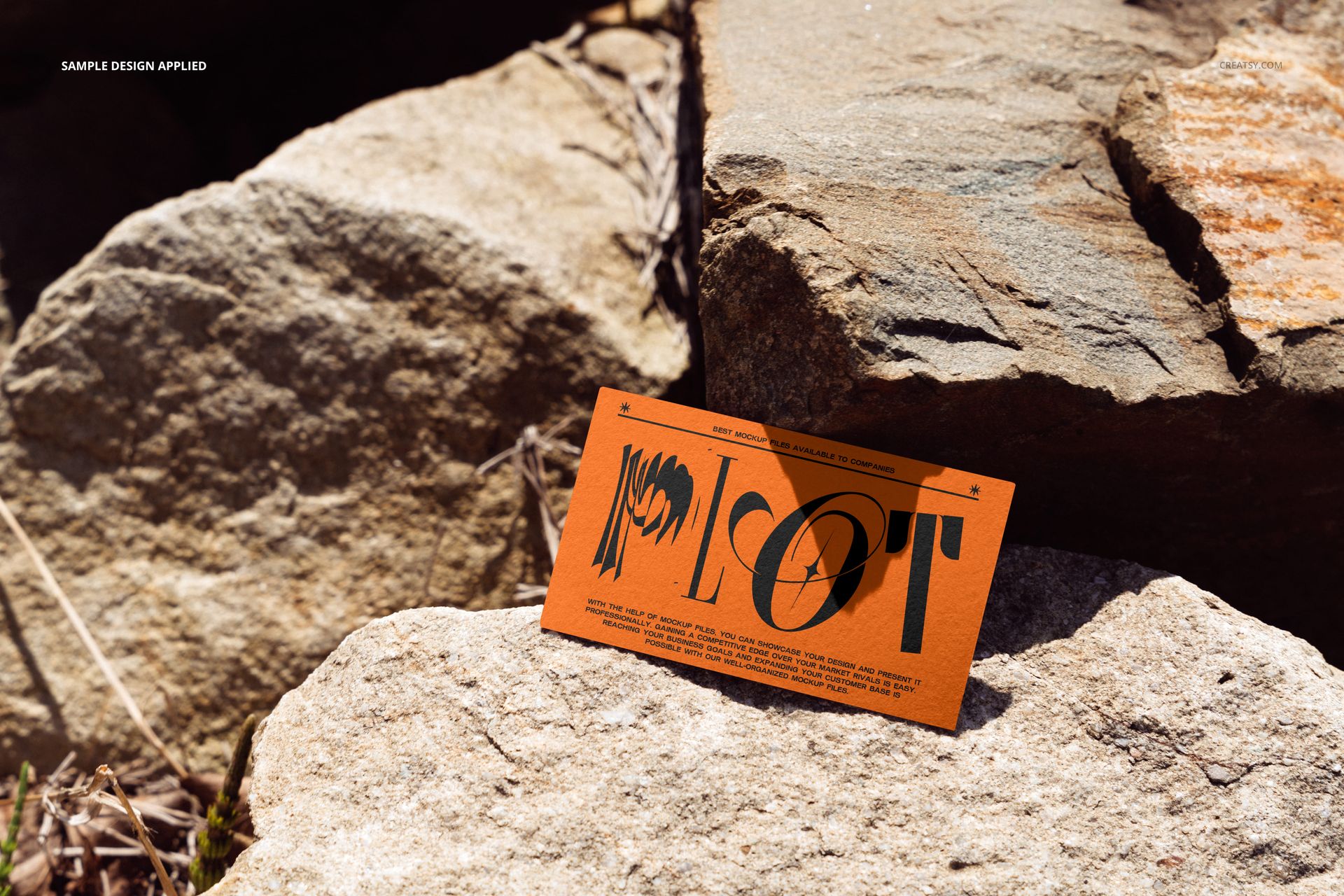 Orange business card featuring graphic design and text, resting on textured rocks outdoors, PSD mockup scene.