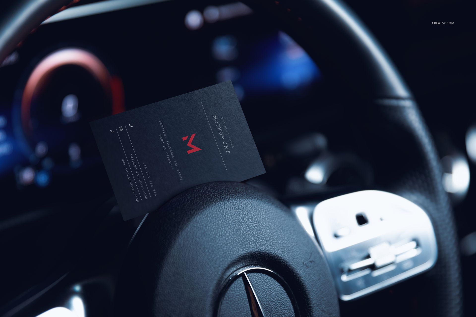 Black automotive business card mockup resting on a car steering wheel, close-up view with dashboard in background.