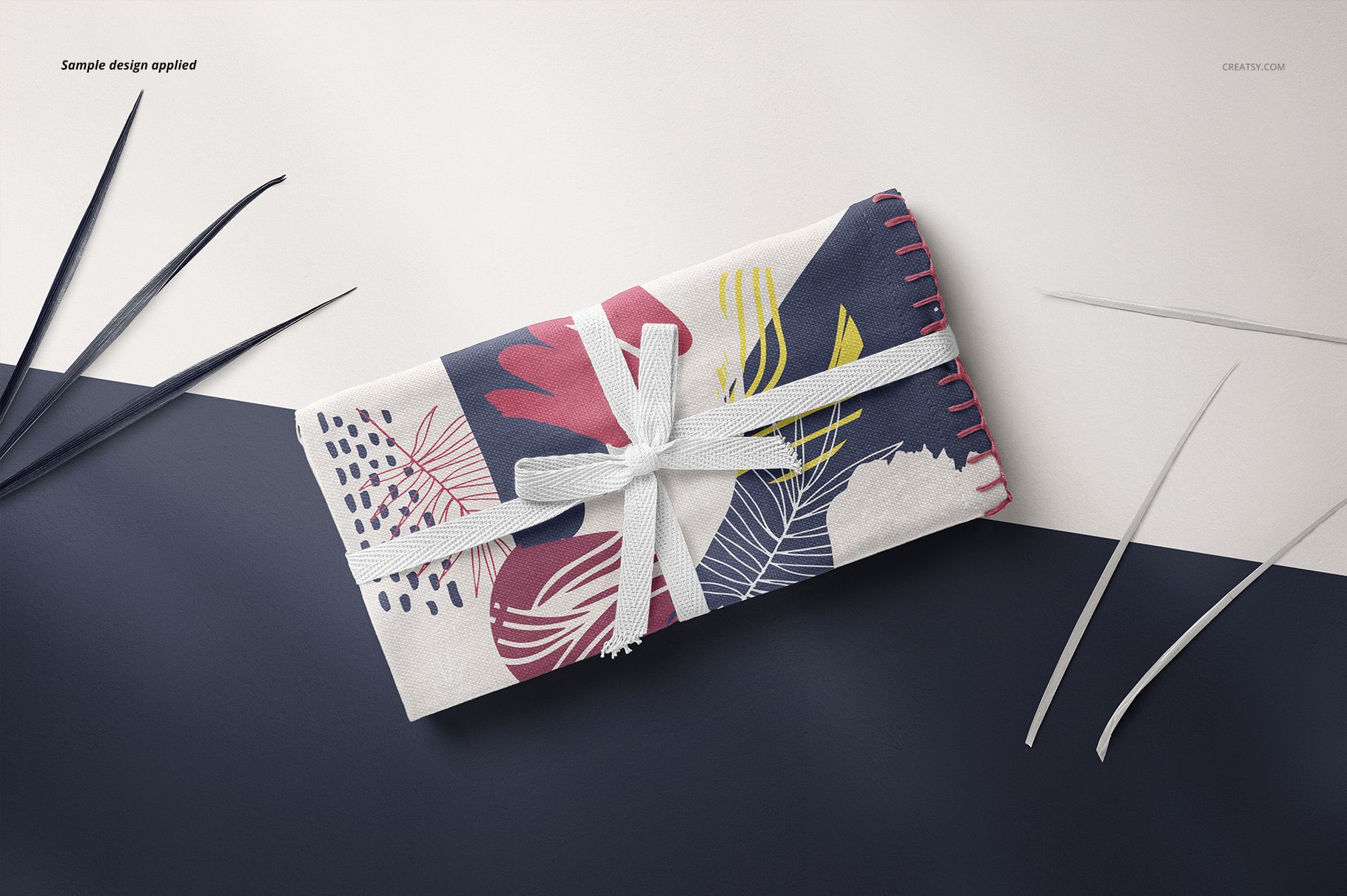 Folded linen fabric mockup featuring a white ribbon, abstract leaf pattern in blue, pink, and yellow tones, top view.