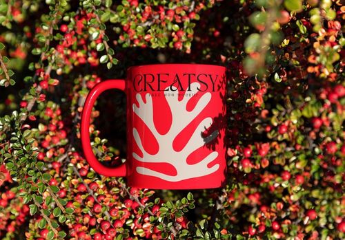 PSD mockup of a red coffee mug with a white organic motif, nestled in lush branches with clusters of red berries.