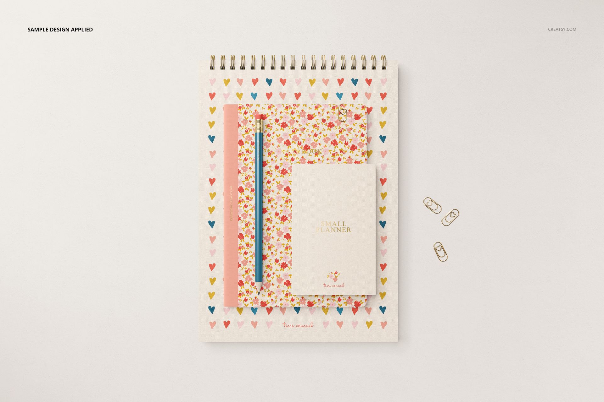 Stationery set mockup featuring a spiral-bound notebook, floral planner, pencil, and paper clips on a light background.