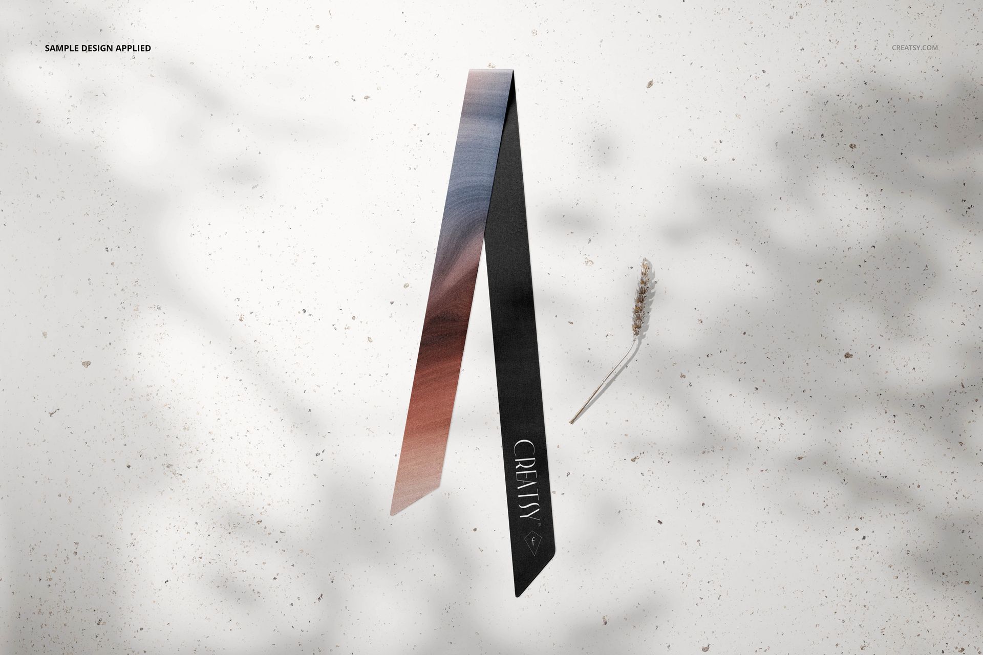 Mockup of a silk twilly scarf with a two-tone gradient pattern, positioned upright on a speckled neutral background.