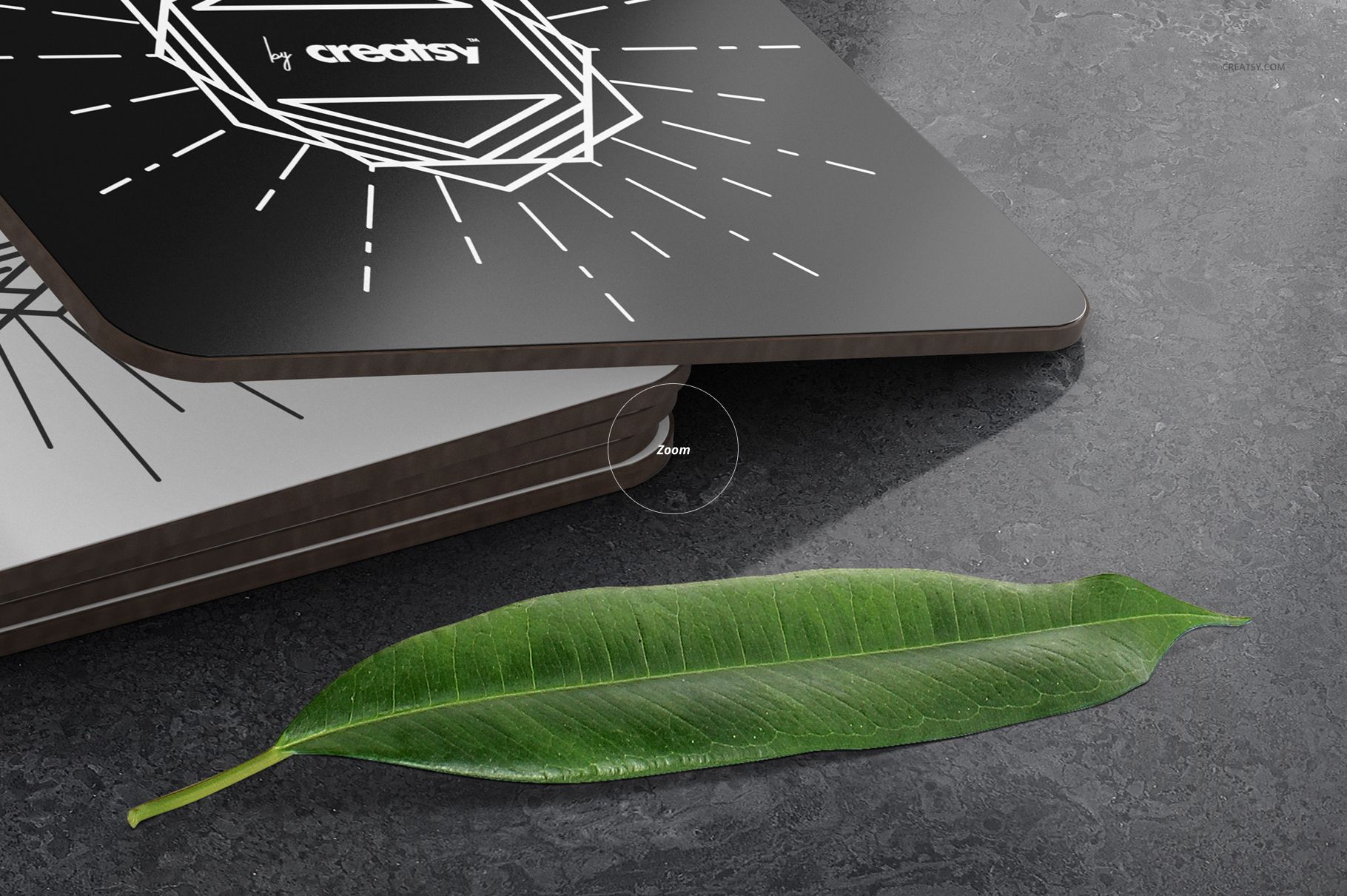 Rectangular coasters mockup showing layered black coasters with white patterns, next to a green leaf on stone.
