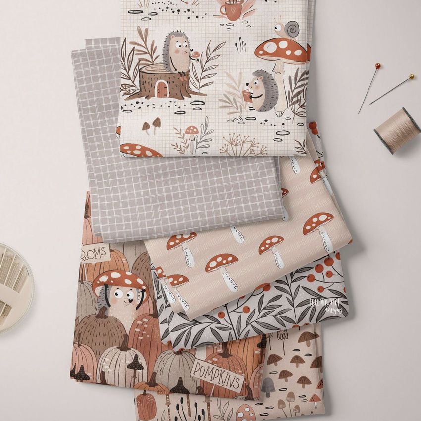 Folded fabrics mockup featuring five pieces of cloth with whimsical woodland and geometric patterns in earthy tones on a light surface.