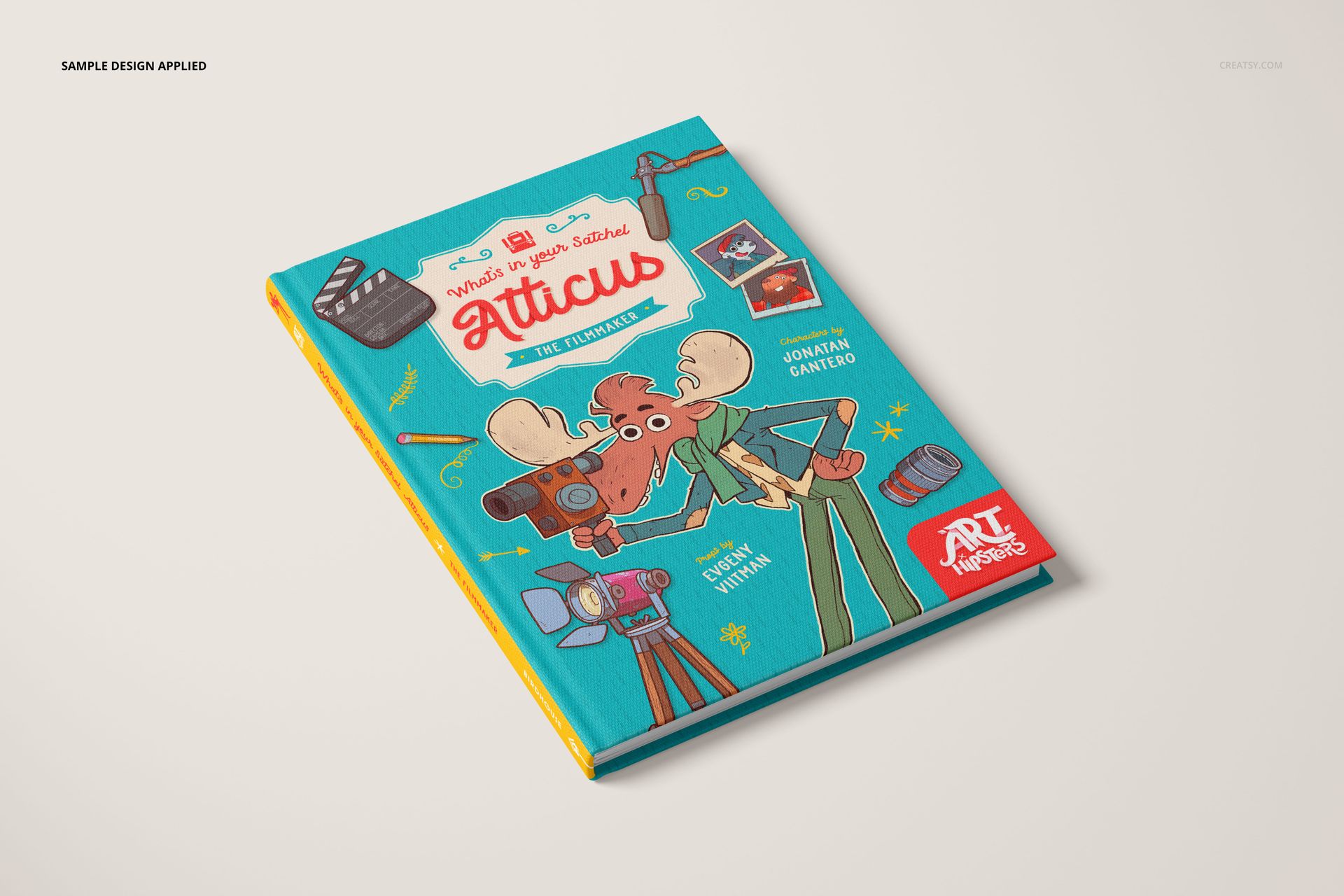 PSD mockup of a hardcover book with a teal cloth cover, playful cartoon artwork, and visible spine, displayed at an angle.
