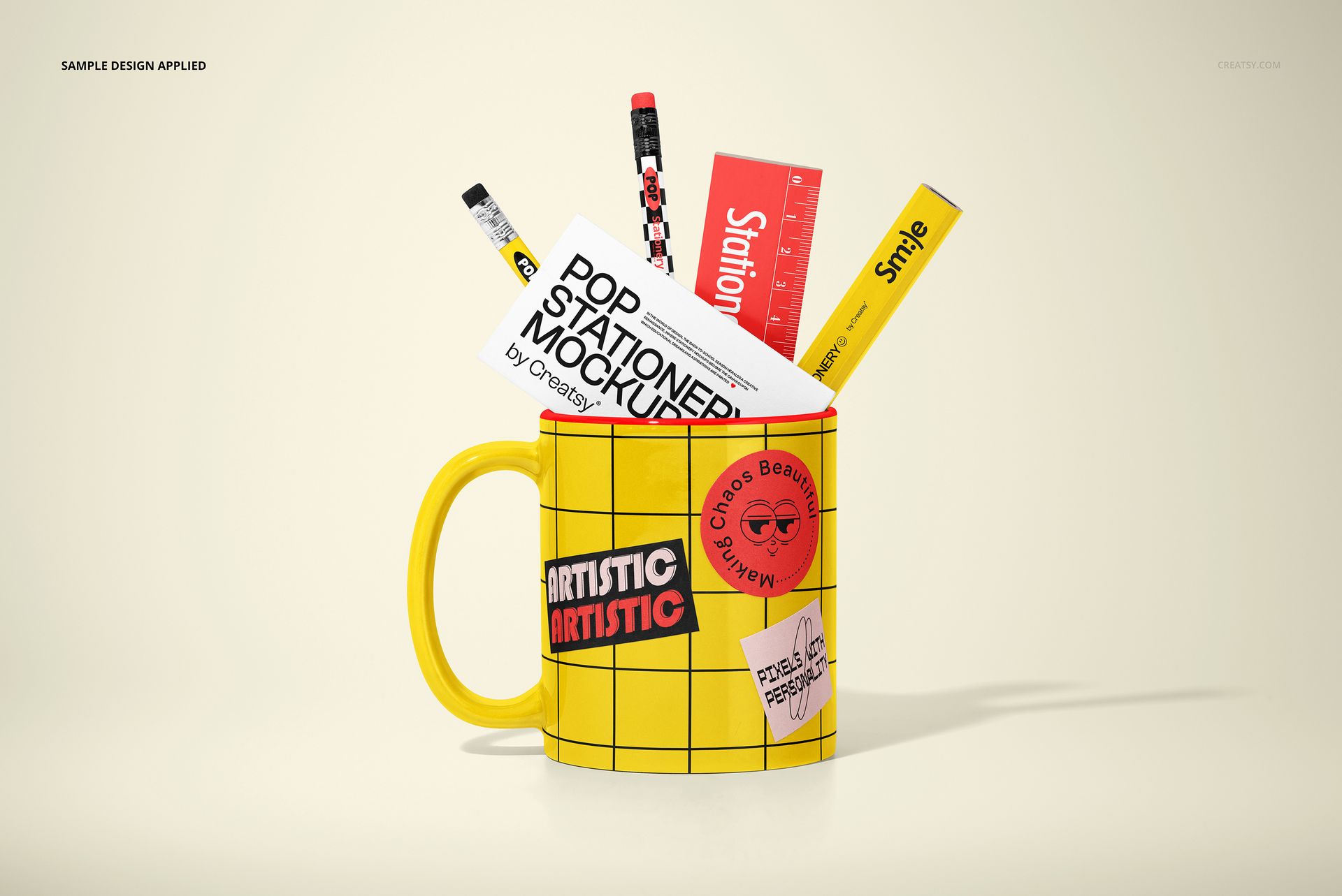 Front view of a mockup featuring a yellow mug with geometric design filled with stationery items on a neutral surface.