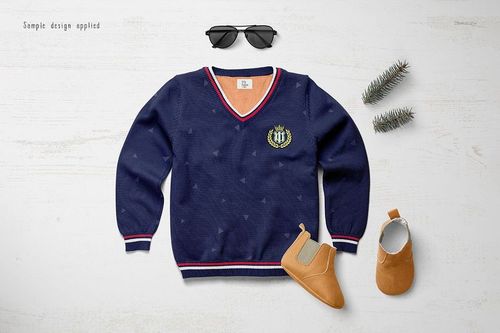 Flat lay of a boys sweater mockup in navy blue with triangle pattern, paired with tan shoes and pine sprigs on a light surface.