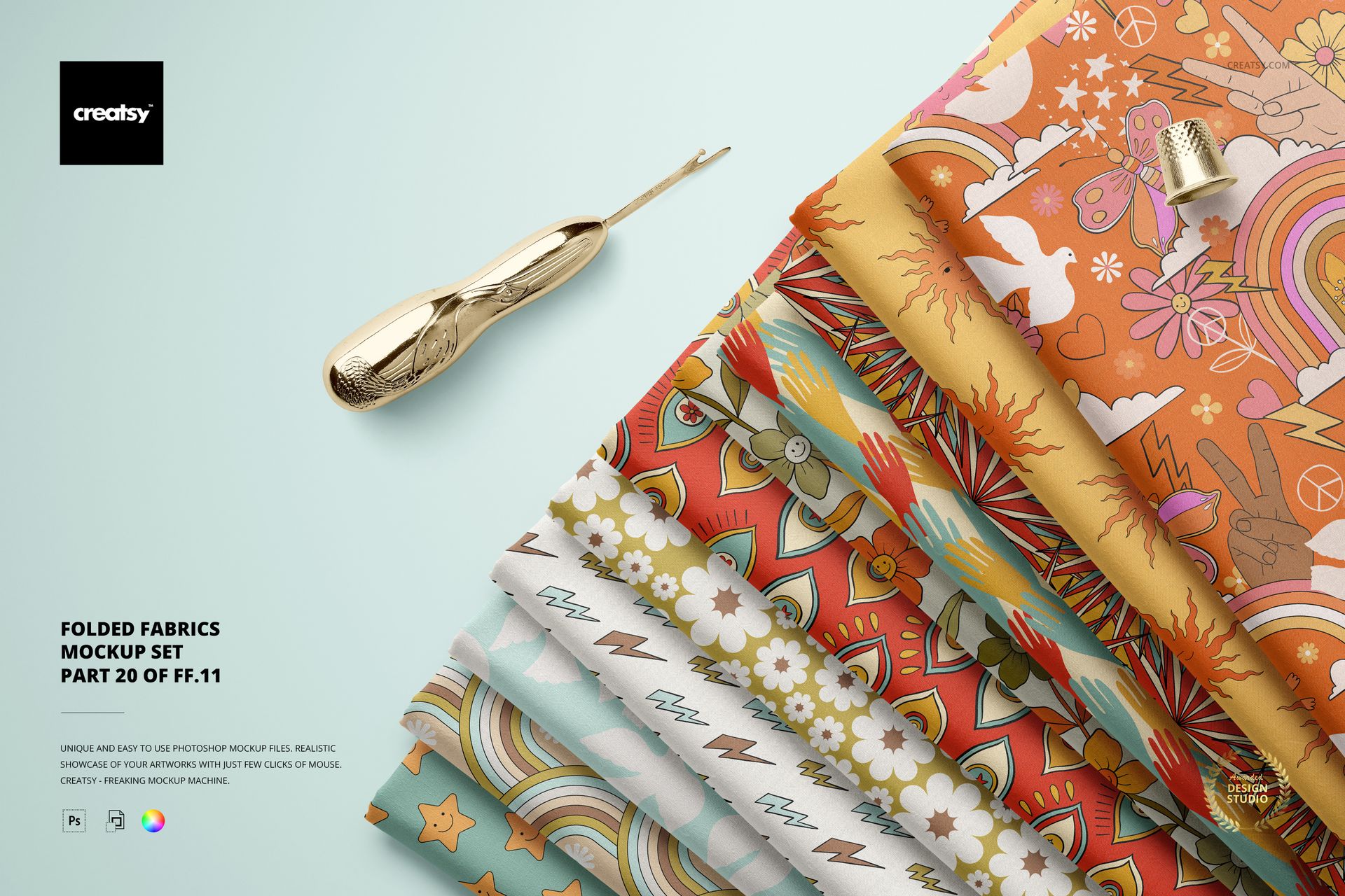 Folded fabric mockup featuring various vibrant designs, viewed from above, with a metallic sewing tool beside the stack.