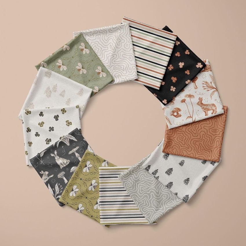 Folded fabrics mockup showing twelve patterned fabric squares arranged in a circle on a beige surface, viewed from above.