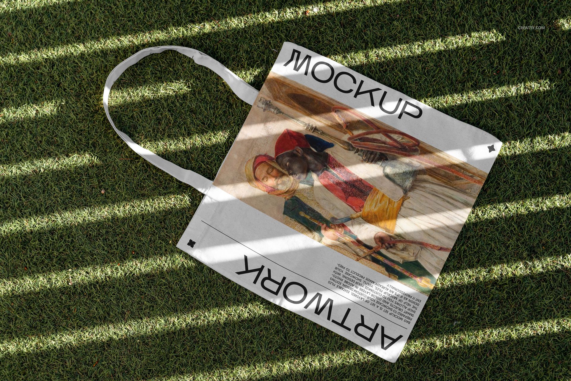 Outdoor tote bag mockup with a colorful artwork print, placed on sunlit grass with diagonal shadow lines.