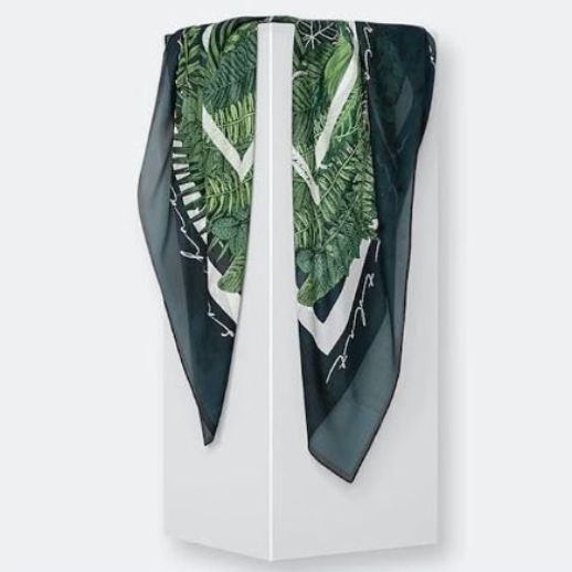Silk scarf mockup draped over a tall white pedestal, featuring a green botanical pattern and dark borders on a plain background.