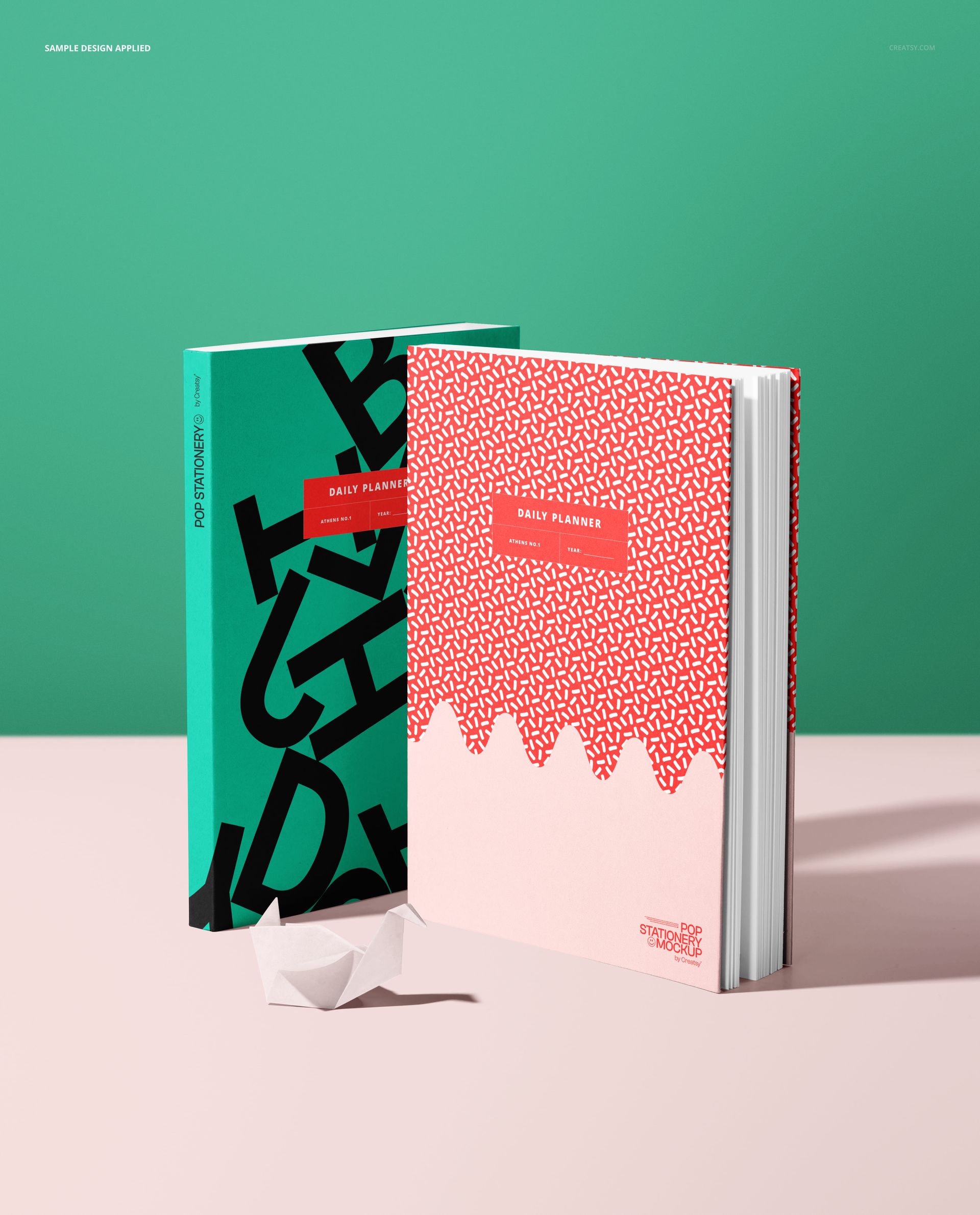 Stationery mockup showing two vertical planners, contrasting cover designs, and a white origami swan on a light pink tabletop.