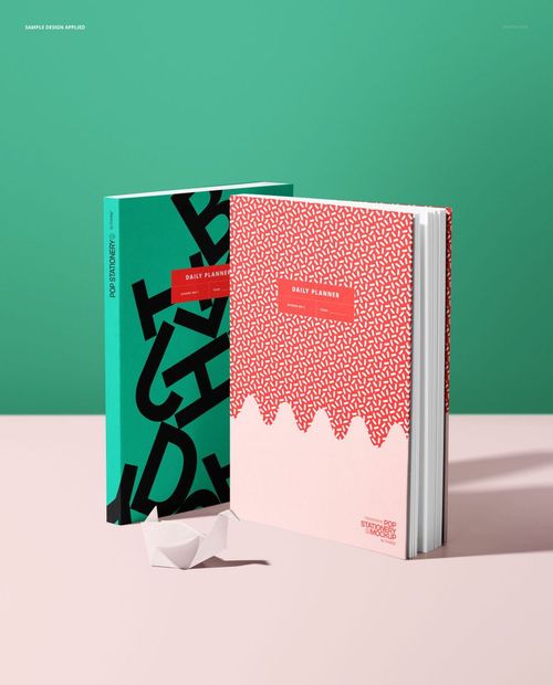 Stationery mockup showing two vertical planners, contrasting cover designs, and a white origami swan on a light pink tabletop.