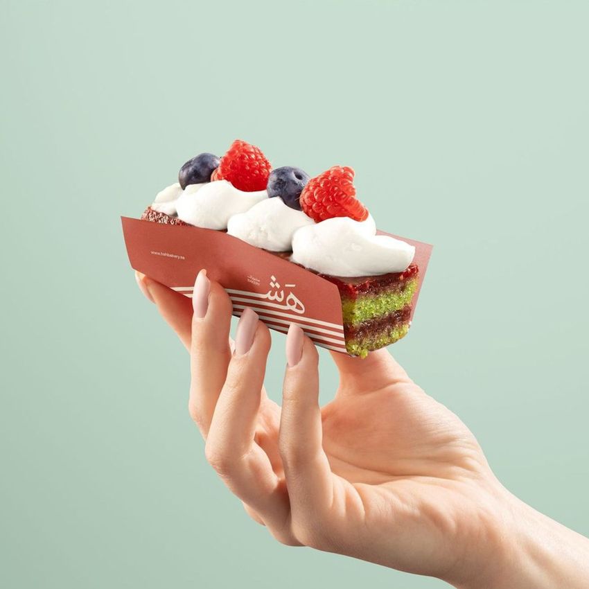 Dessert mockup featuring a hand displaying a pastry in custom food safe paper with a red pattern and fresh berries, minimal background.