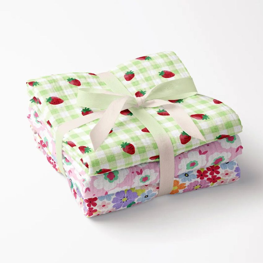 Crinkle muslin swaddle blanket mockup featuring two folded blankets, one with a green checkered strawberry pattern and one with colorful flowers, tied with a cream ribbon on a white background.