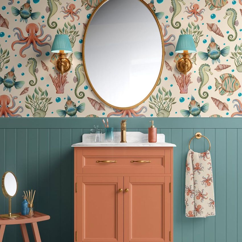 Bathroom cabinet wallpaper mockup showing a coral-colored vanity, oval mirror, and vintage ocean creature wallpaper.