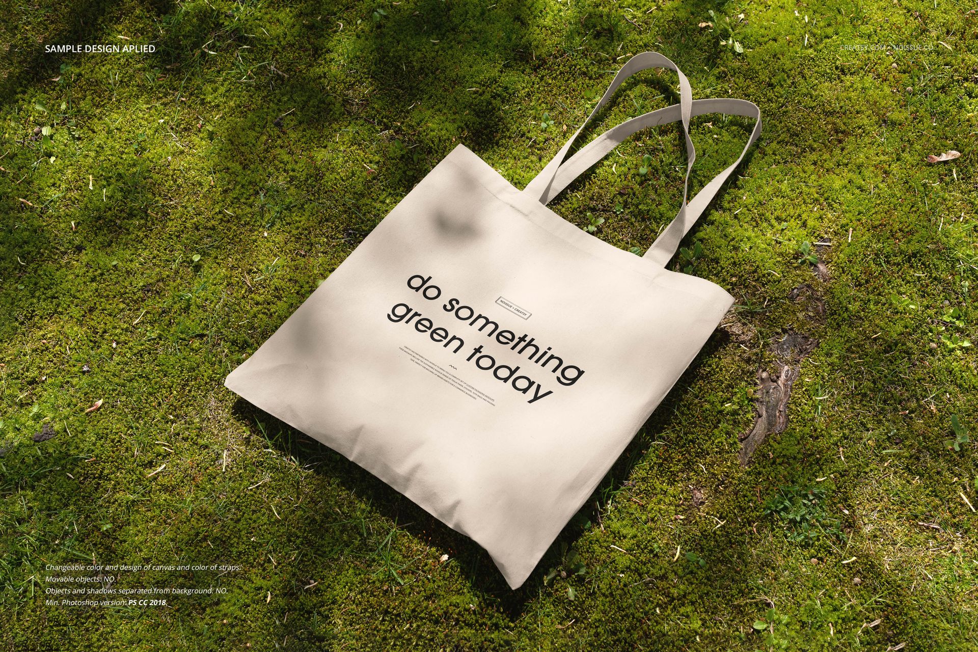 Neutral tote bag mockup lying on green grass, shown from above with long handles and natural lighting.