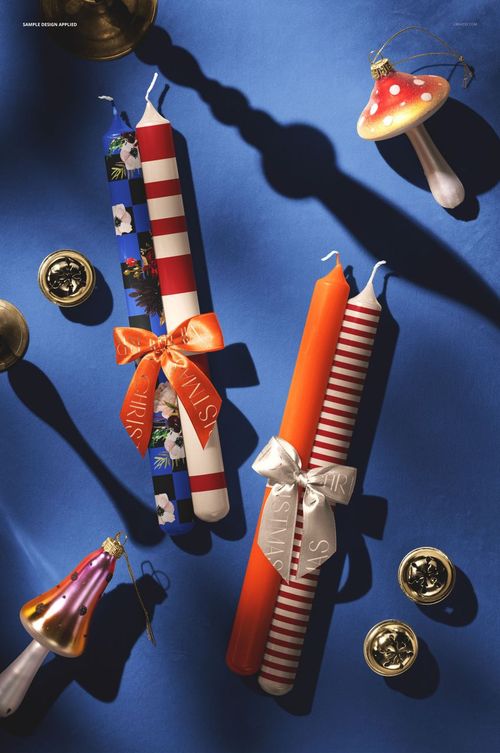 Festive candle mockup featuring red and white striped and floral candles, ribbons, and Christmas decorations on a blue background.