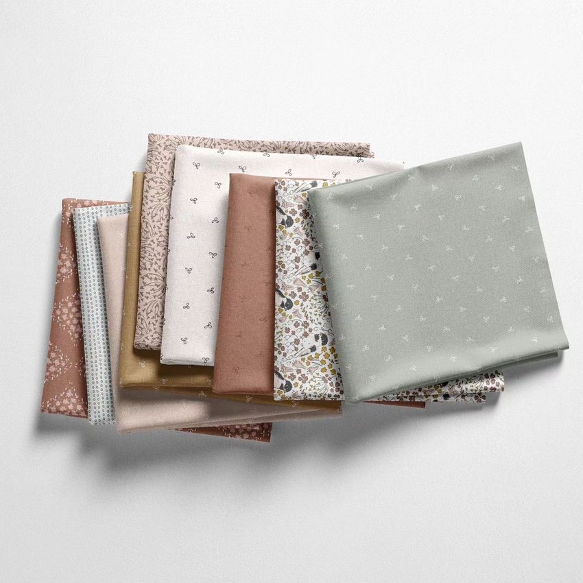 Fabric stack mockup showing neatly folded cotton fabrics in soft pastel tones with various floral and geometric patterns on a light surface.