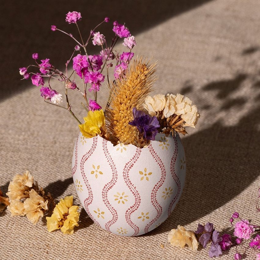 Painted Easter egg shell mockup used as a vase, holding dried flowers and wheat, on a textured fabric surface.