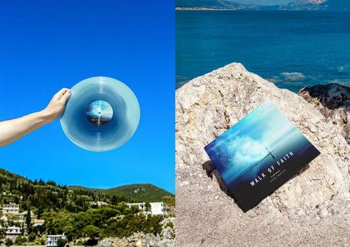 PSD mockup of a vinyl record and album cover placed on rocks by the sea, with vivid blue water and sky.