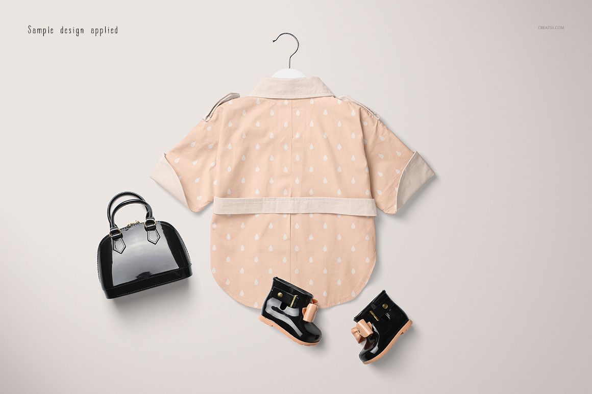 Front view of a baby coat mockup in light peach with white dots, displayed on a hanger with black shoes and a handbag.