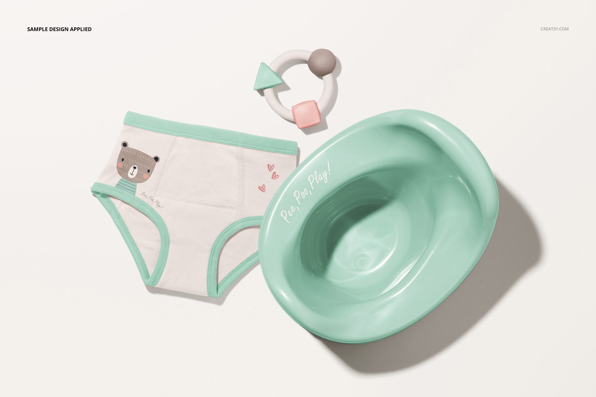 Toddler training pants mockup set featuring white pants with mint trim and bear design, mint potty, and teething toy, top view.