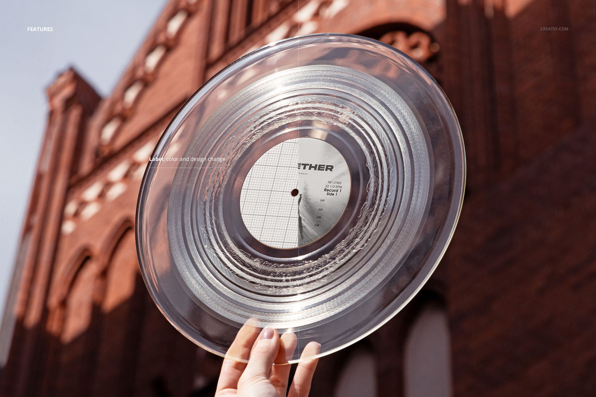 Transparent vinyl record mockup held up against a historic brick building, shown from a front perspective in daylight.