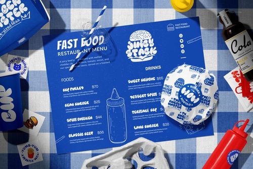 Vegan burger bar packaging mockup with branded wrappers, menu, drink cup, and cola bottle on a blue checkered table.