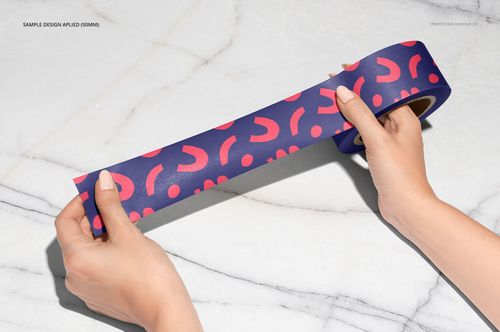 Close-up view of a decorative packing tape mockup featuring bold pink shapes on a dark purple tape, held by two hands.