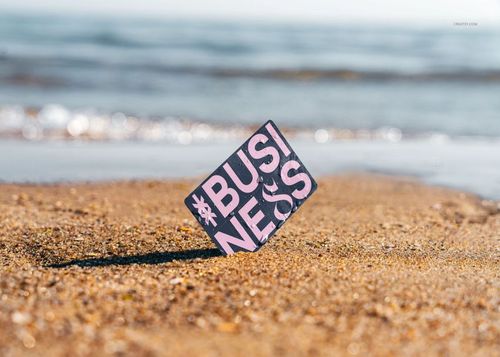 Rectangular business card mockup standing upright on sandy beach with blurred ocean waves in the background.
