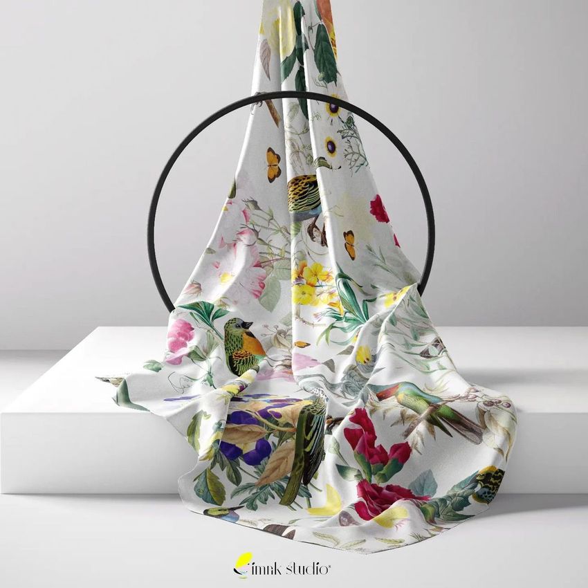 Silk scarf mockup draped over a black circular frame, featuring a colorful abstract floral and bird pattern on a white background.