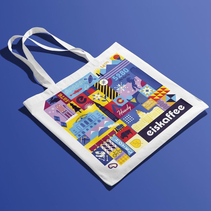 Tote bag mockup featuring a white fabric bag with colorful geometric and graphic illustrations, photographed on a blue background.