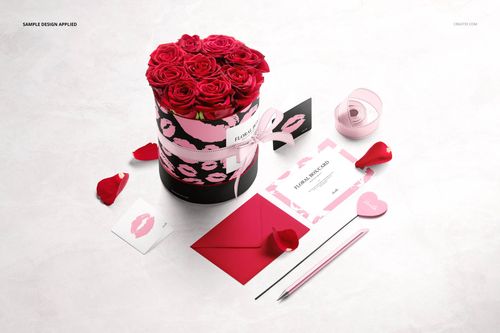 Round floral box mockup with pink roses, surrounded by stationery items, ribbon, and rose petals on a light surface.