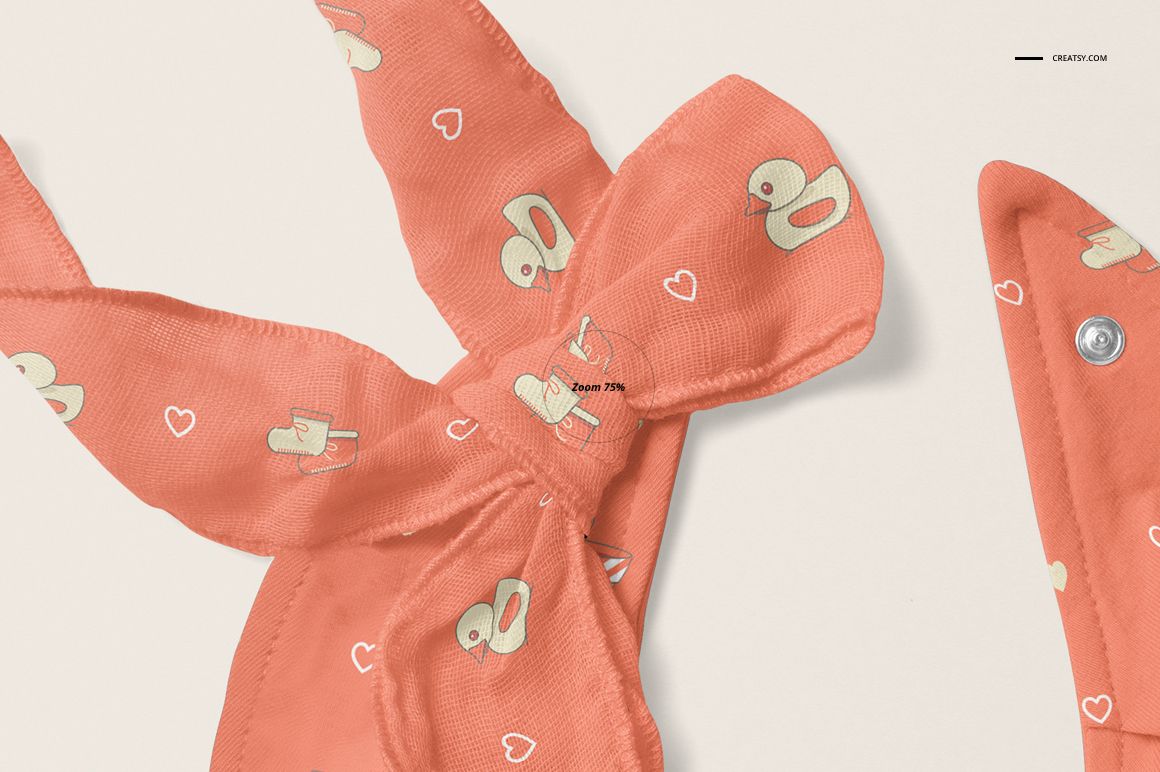 Coral baby bandana bib mockup featuring cartoon duck and heart motifs, shown in close-up on a neutral surface.