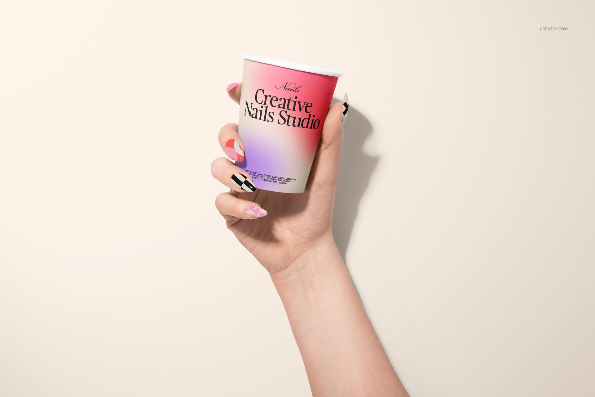 Hand with colorful nail art holding a white cup with gradient pink label, shown against a light background in front view.